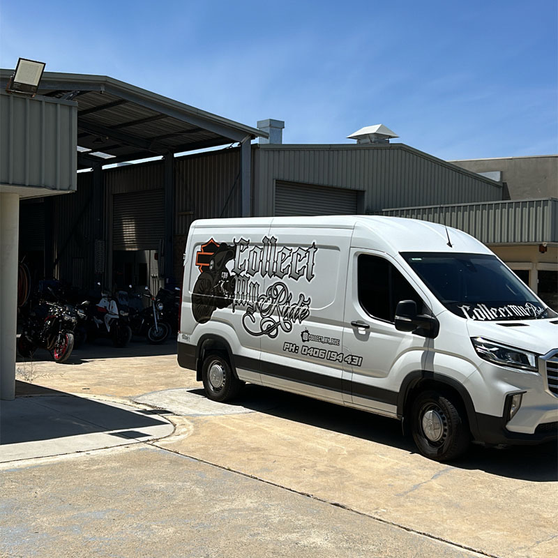 Branded white van parked beside a shed with motorcycles inside