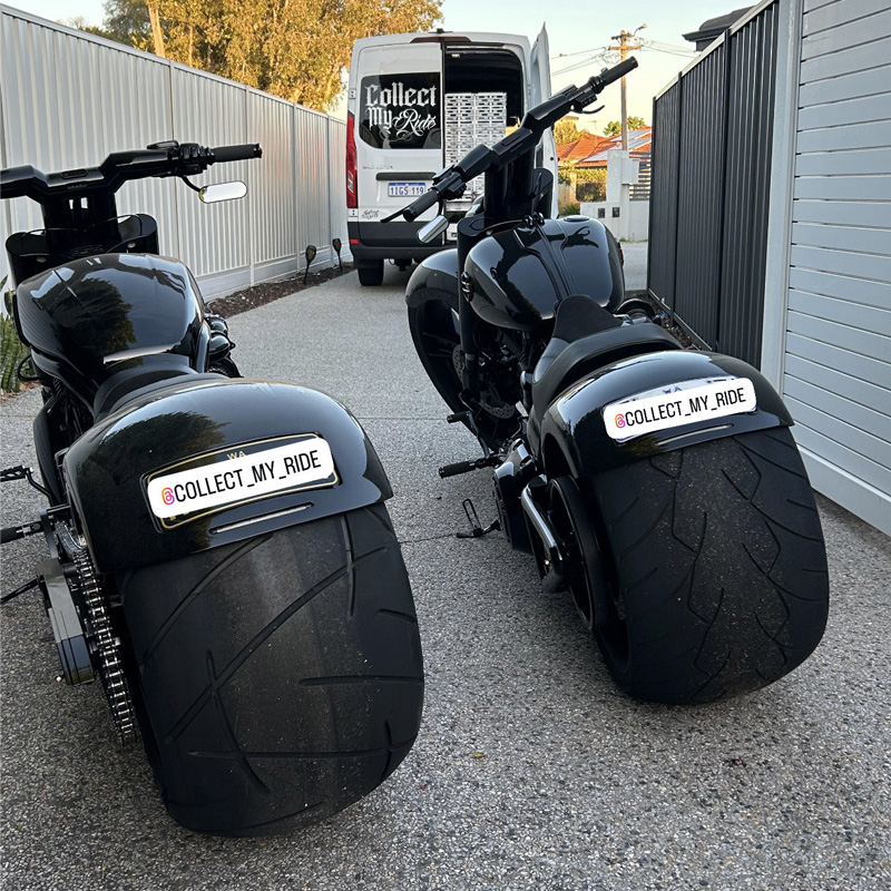 Rear view of two black custom motorcycles with wide tyres in a driveway