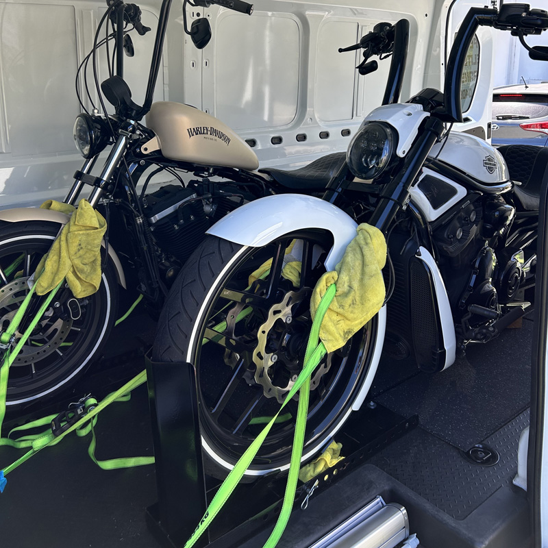Beige-tanked Harley-Davidson and a white motorcycle strapped down inside a van